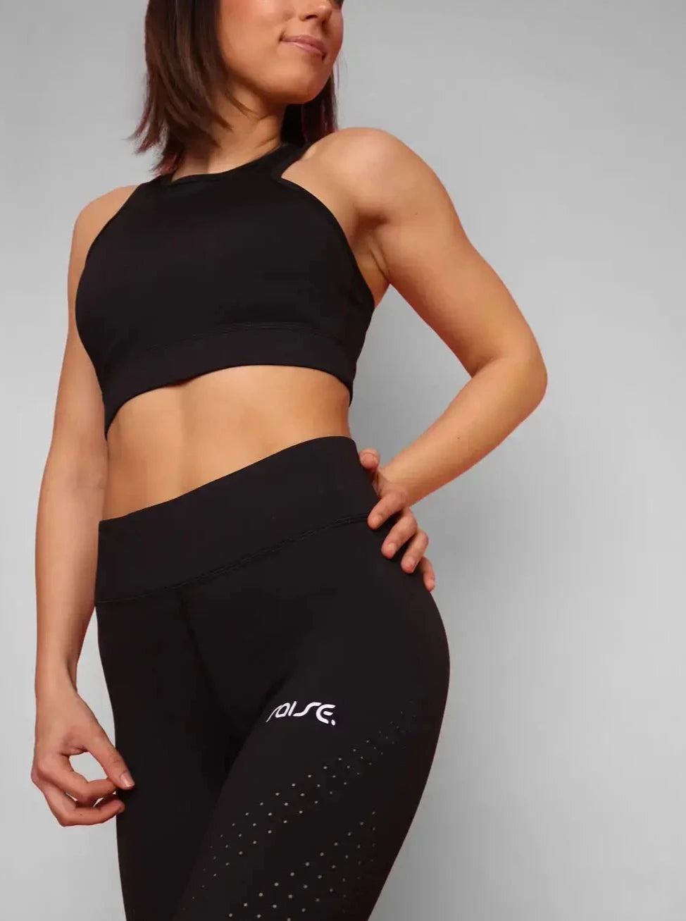 Sportliche Frau posiert in schwarzer Sport Leggings und schwarzem Sport BH von raise Sportswear