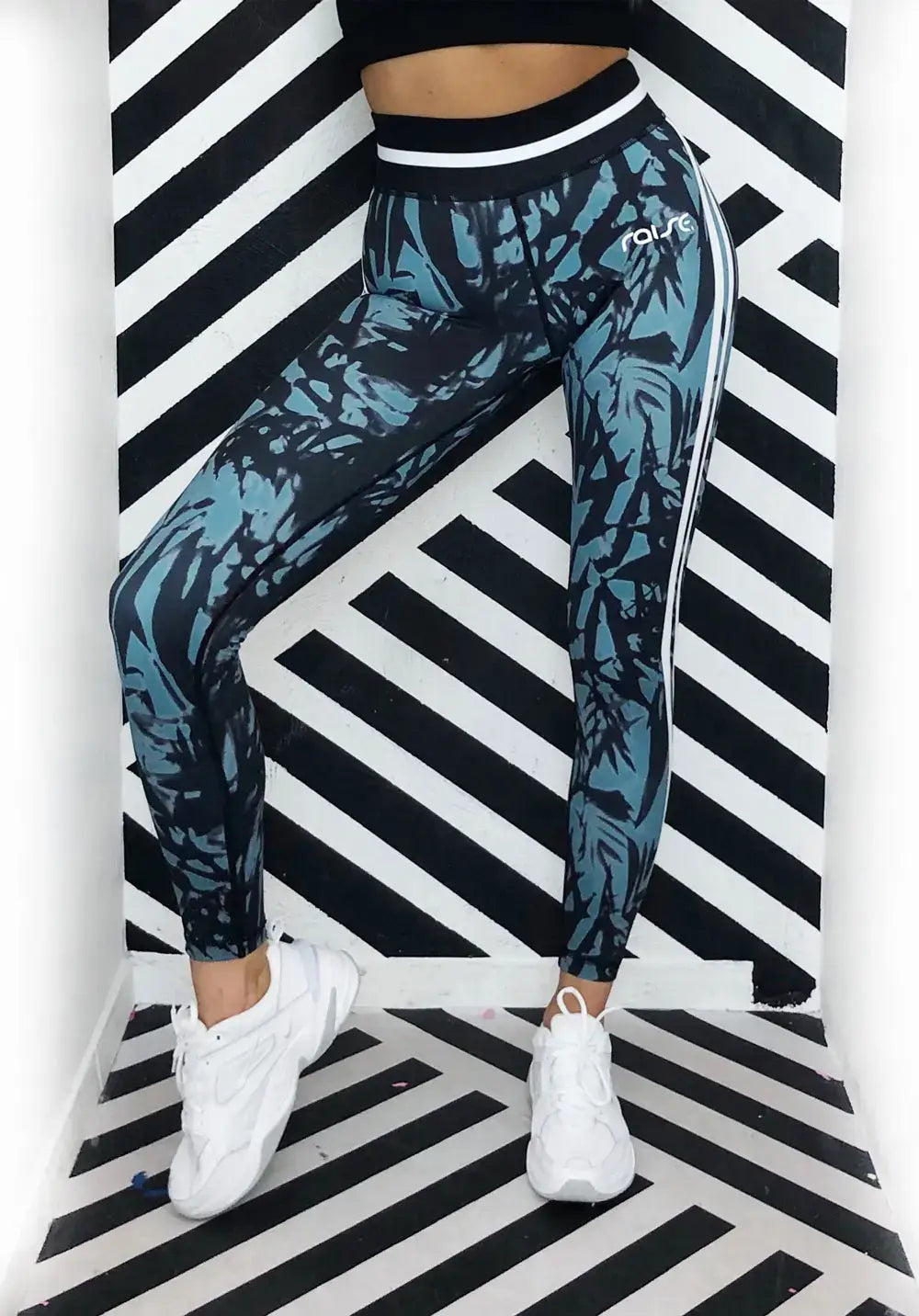 Unterkörper von schlanker Frau in grün schwarz weißer Sport Leggings von raise Sportswear vor schwarz weiß gestreiftem Hintergrund