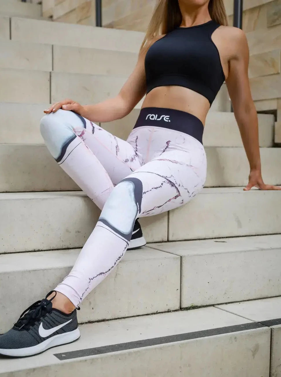 Blonde sportliche Frau in rosa Sport Leggings und schwarzem Sports Bra von raise Sportswear sitzt draußen auf Treppenstufe