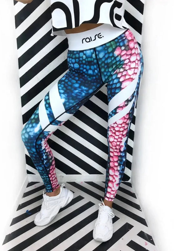 Beinausschnitt von schlanker Frau in bunter Sport Leggings und weißem Crop Top von raise Sportswear vor schwarz weiß gestreifter Wand