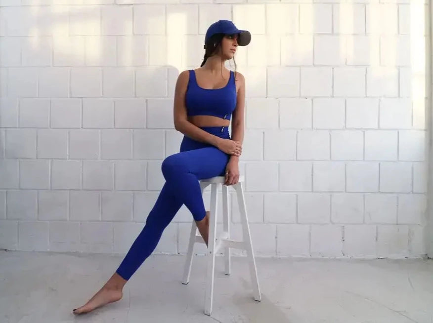 Brünette Frau in blauer Seamless Sport Leggings und blauem Sports Bra von raise Sportswear sitzt auf Hocker