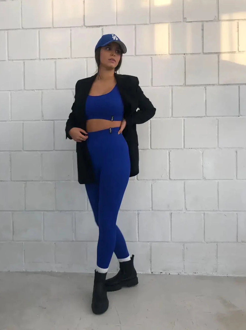 Brünette Frau in blauer Seamless Sport Leggings von raise Sportswear und schwarzem Blazer posiert vor weißer Wand