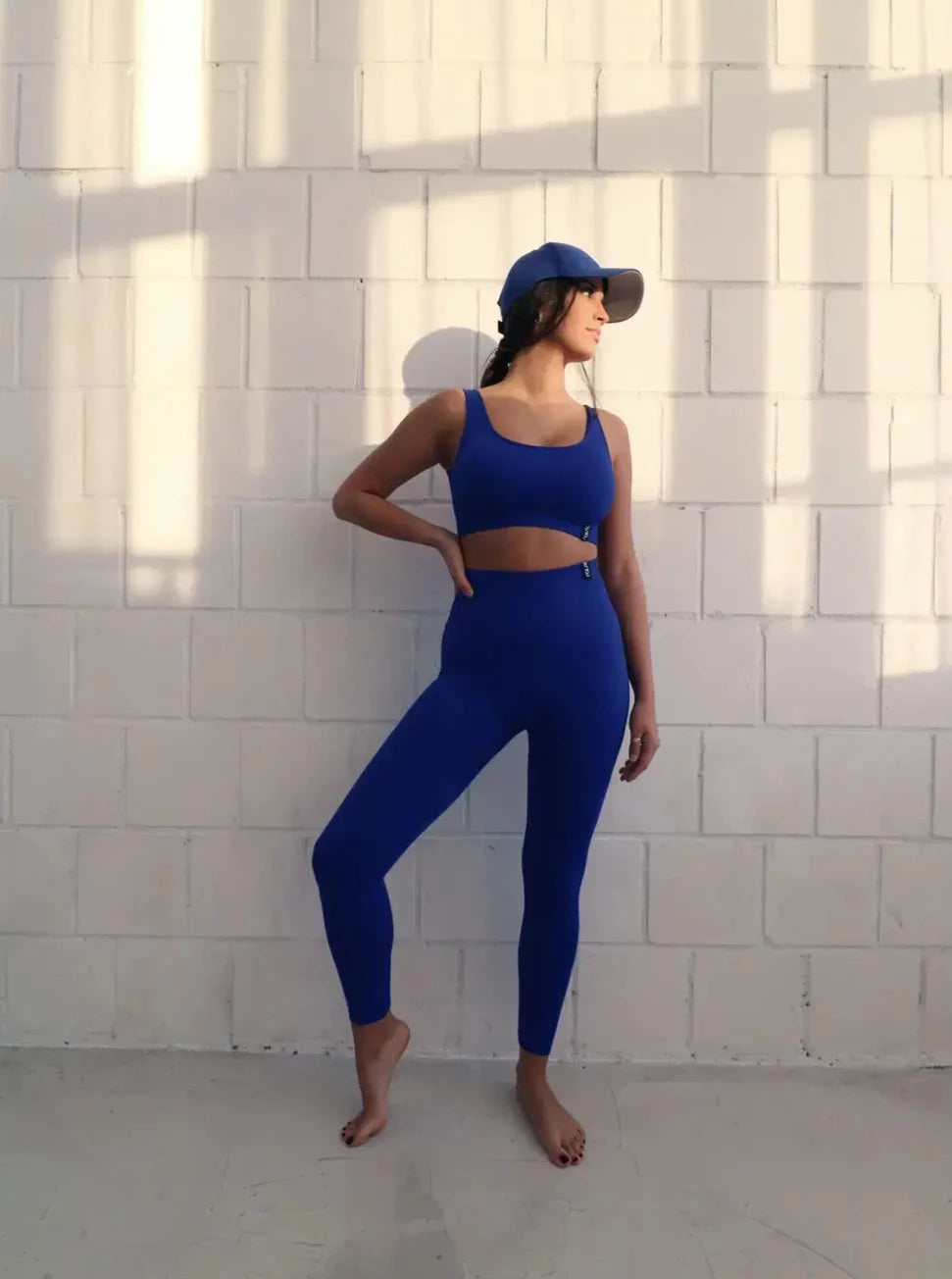 Brünette Frau in blauer Seamless Sport Leggings und blauem Sports Bra von raise Sportswear posiert vor weißer Wand
