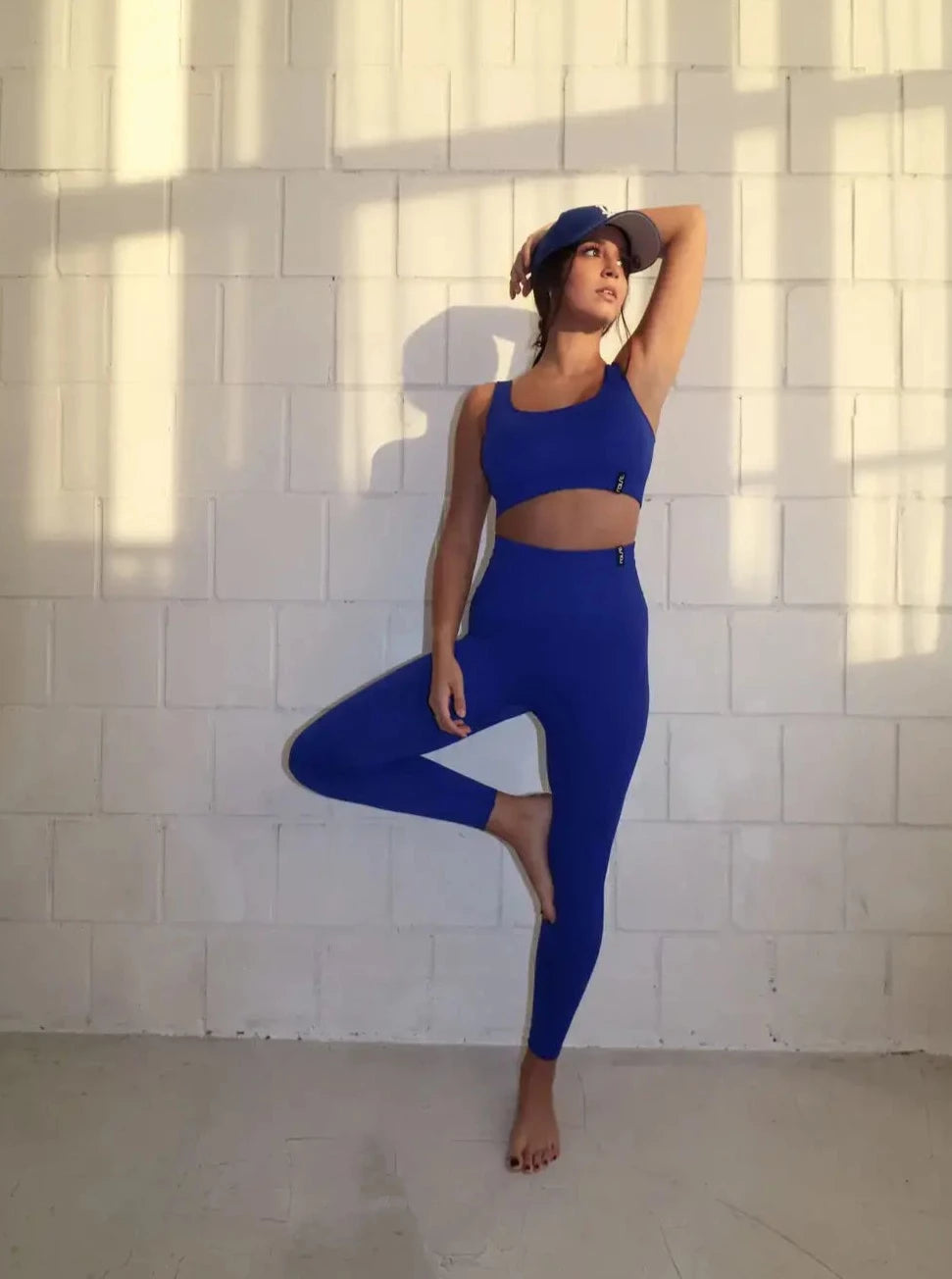 Brünette Frau in blauer Seamless Sport Leggings und blauem Sports Bra von raise Sportswear posiert vor weißer Wand