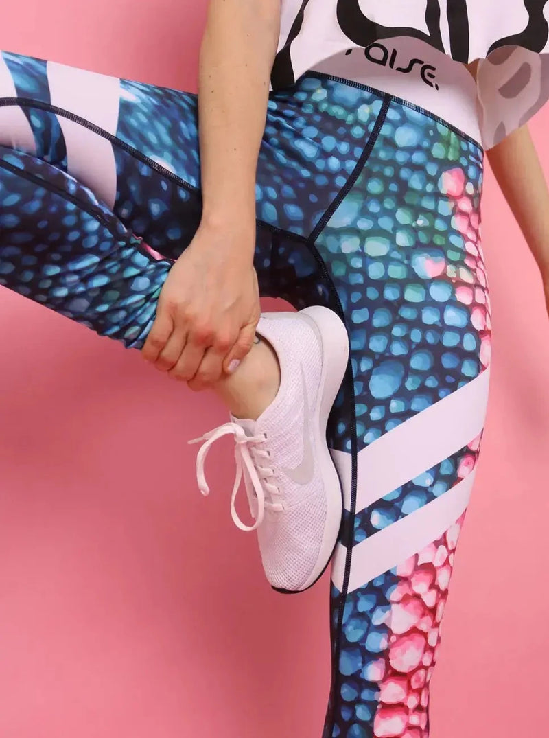 Beine von schlanker Frau in bunter Sport Leggings von raise Sportswear vor rosa Hintergrund
