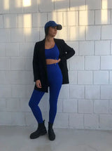 Brünette Frau in blauer Seamless Sport Leggings von raise Sportswear und schwarzem Blazer posiert vor weißer Wand