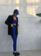 Brünette Frau in blauer Seamless Sport Leggings von raise Sportswear und schwarzem Blazer posiert vor weißer Wand