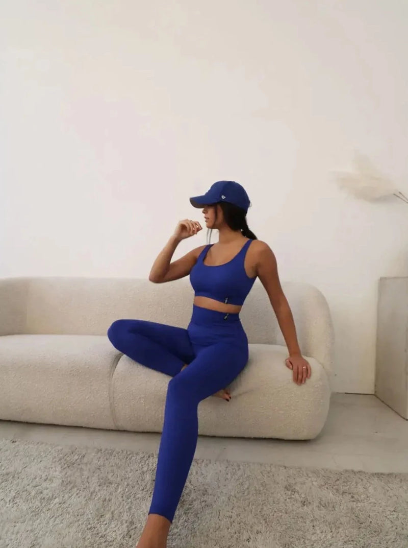 Brünette Frau in blauer Seamless Sport Leggings und blauem Sports Bra von raise Sportswear sitzt auf Sofa