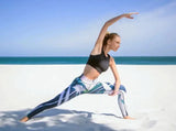 Sportliche Frau in bunter Sport Leggings und schwarzem Sport BH von raise Sportswear macht Yoga am Strand